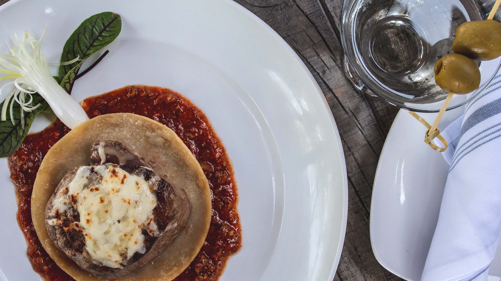 A chile relleno in red sauce, a martini beside it