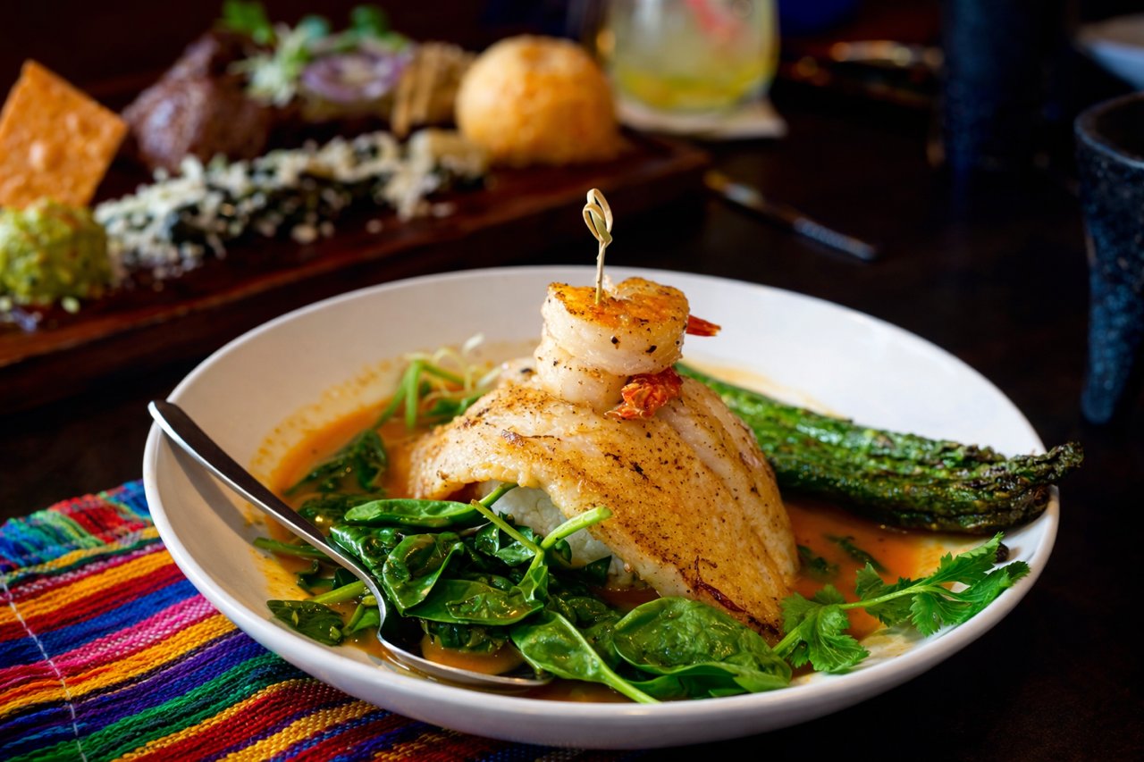 A fish fillet over greens in a red chile broth with a roasted jalapeno