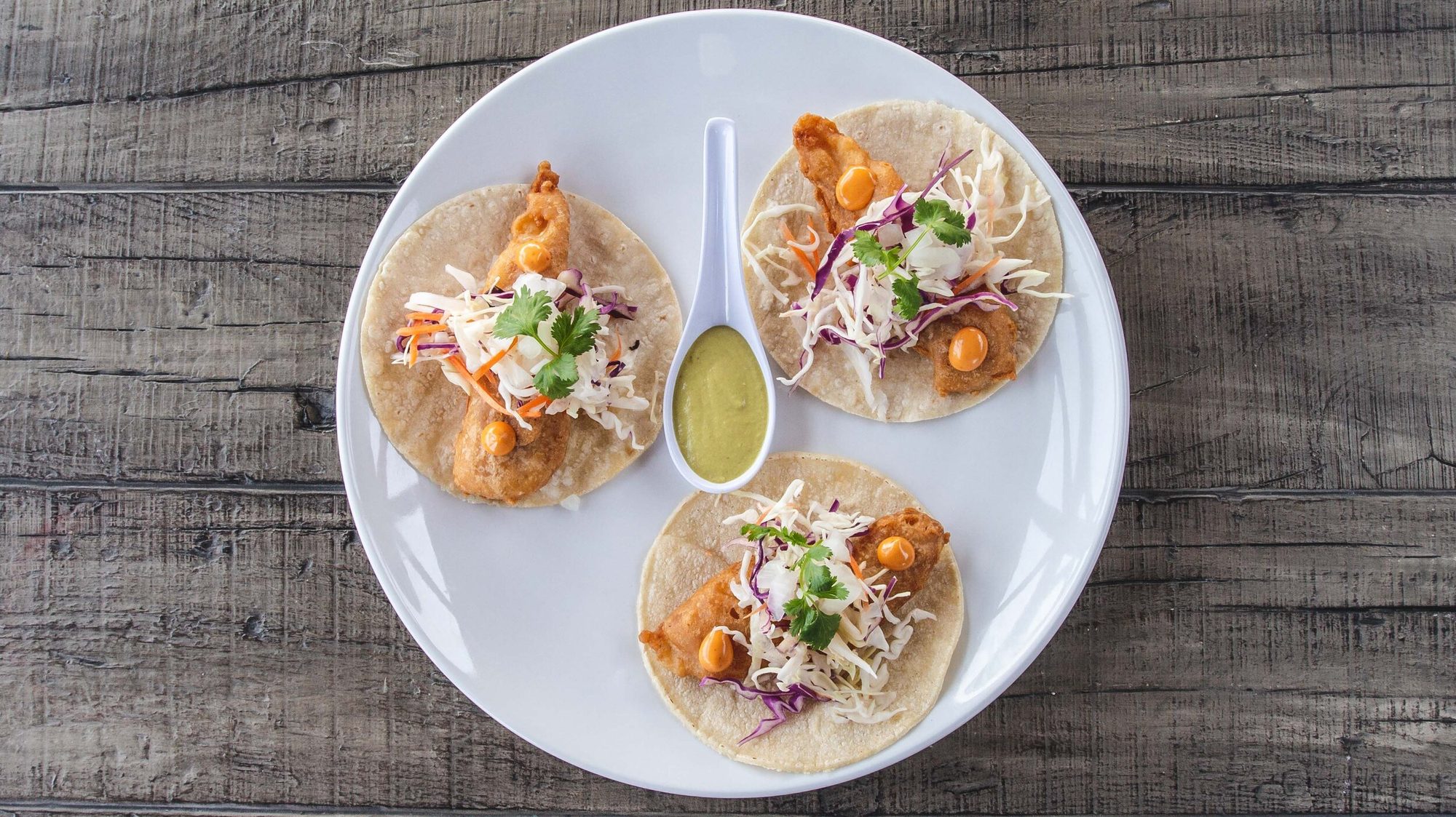 Three fish tacos and a green salsa, seen from above