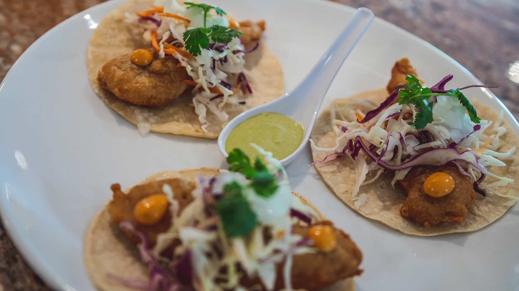 Fish tacos beside a spoon of green salsa