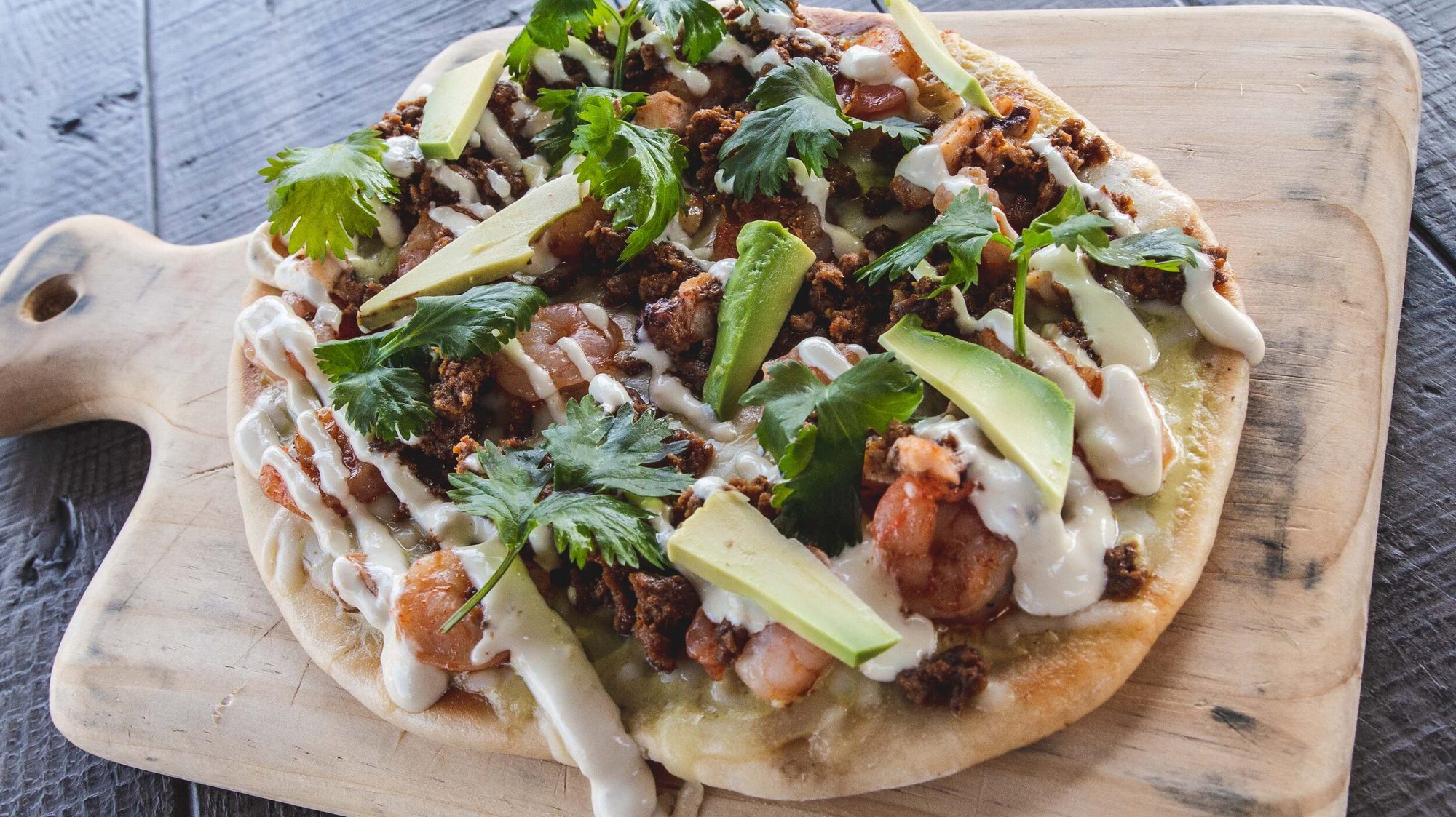 A shrimp flatbread on a wooden board