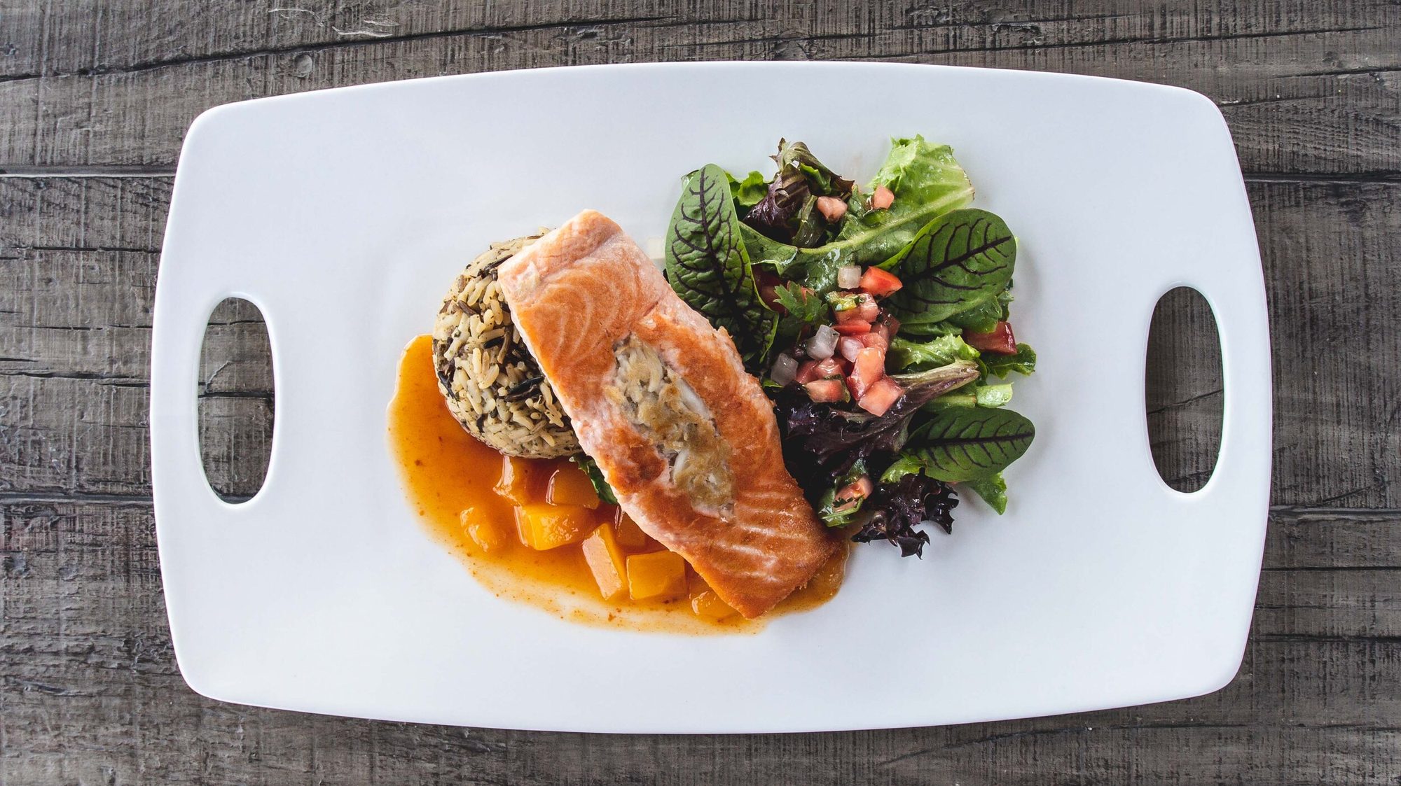 Salmon with wild rice and salad on a white platter