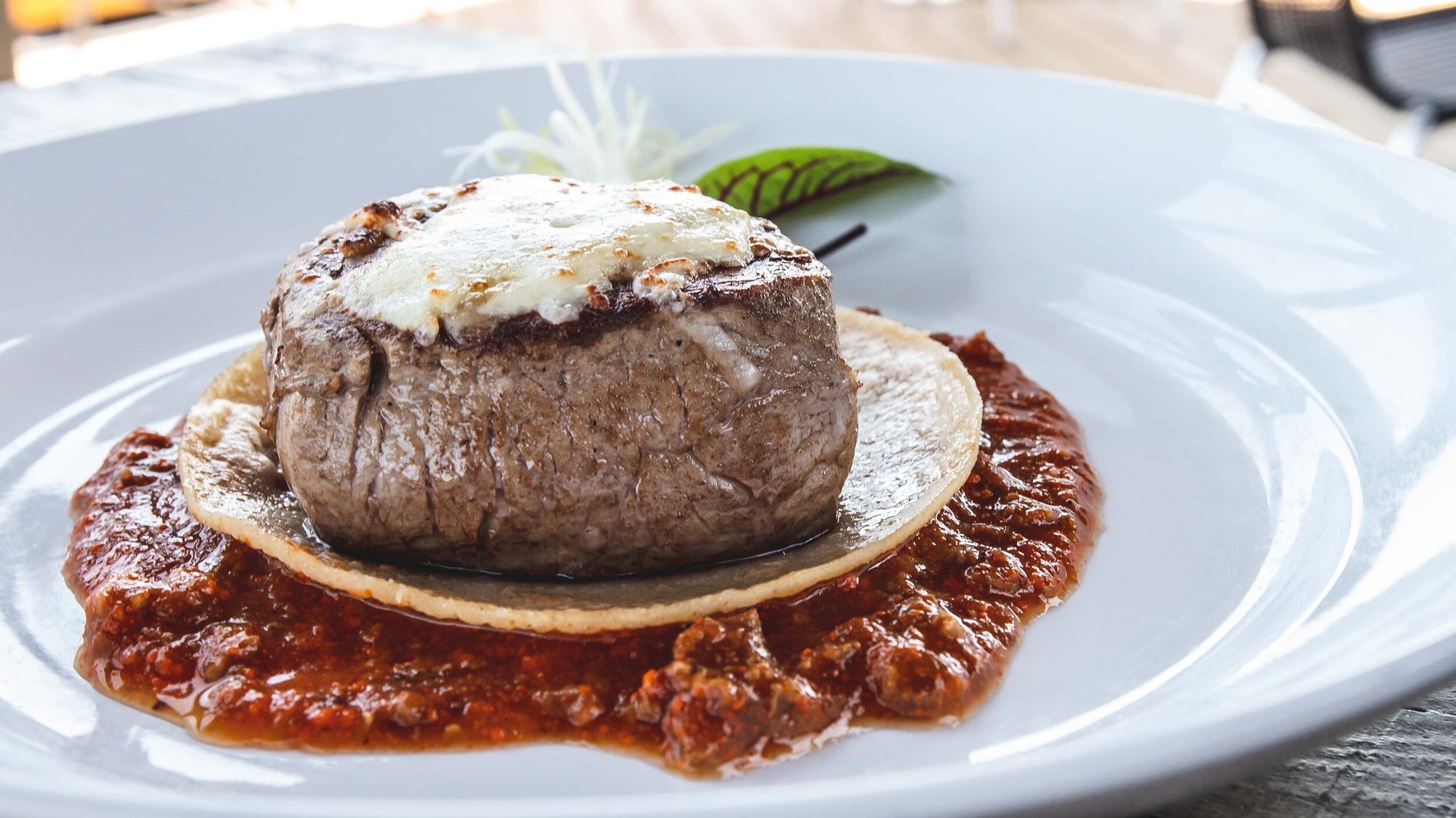 A beef medallion on a tortilla in a red sauce
