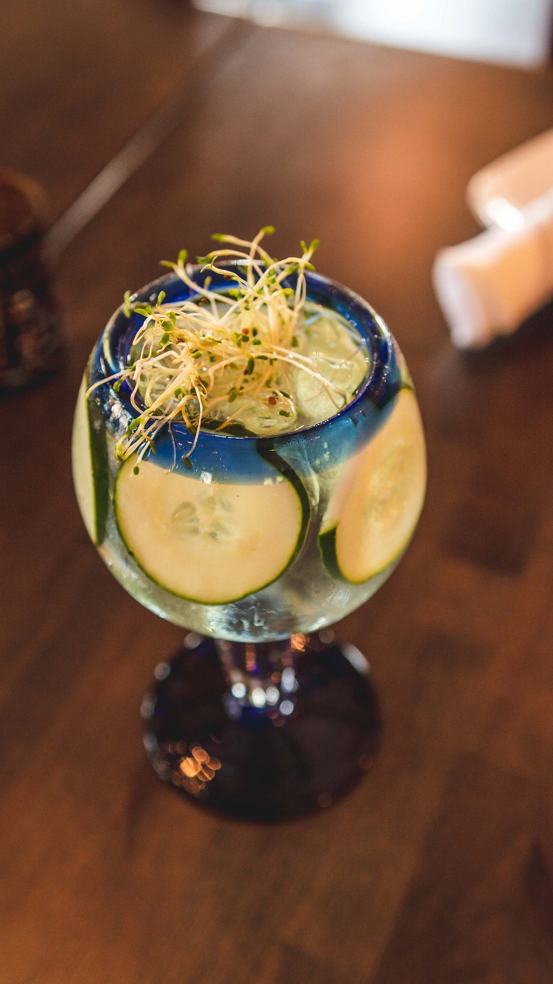 A cocktail in cobalt glass with cucumber and herbs