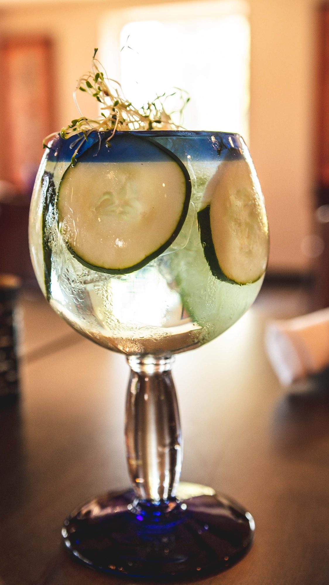 A cucumber cocktail in a cobalt-stemmed glass
