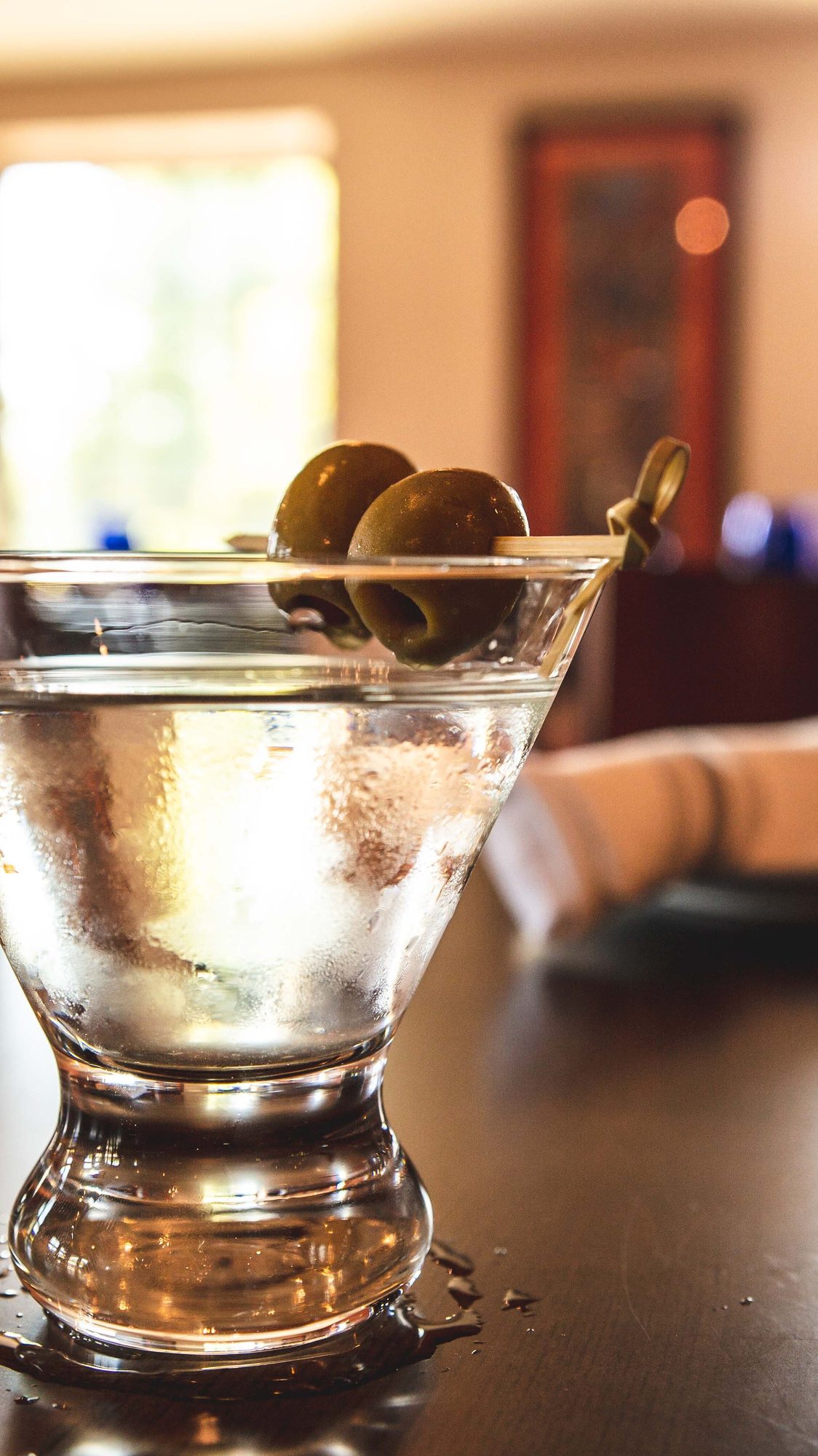 A martini with olives, backlit at the bar