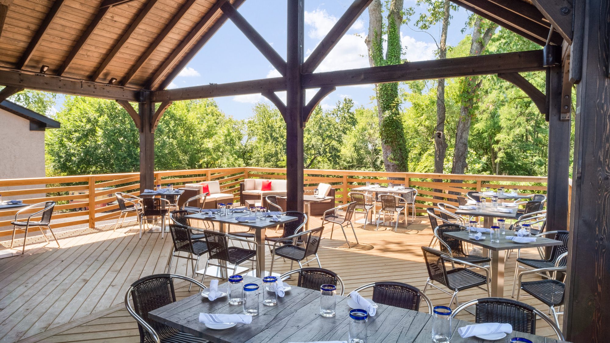 Patio tables laid with glasses, trees beyond the rail
